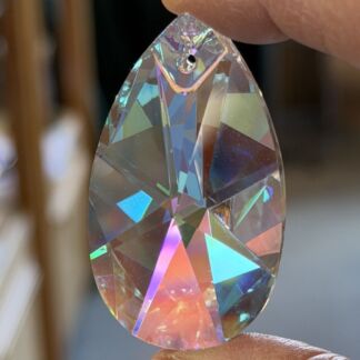 Teardrop-shaped crystal prism held between fingers, showing rainbow-colored facets and a small hole at the top for hanging.