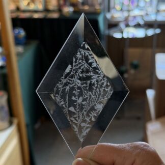 Diamond-shaped glass ornament with an etched leaf pattern, held between fingers.