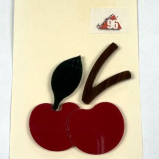Craft collage of two red cherries with a brown stem and dark leaf on a cream card; small logo sticker in upper right corner.